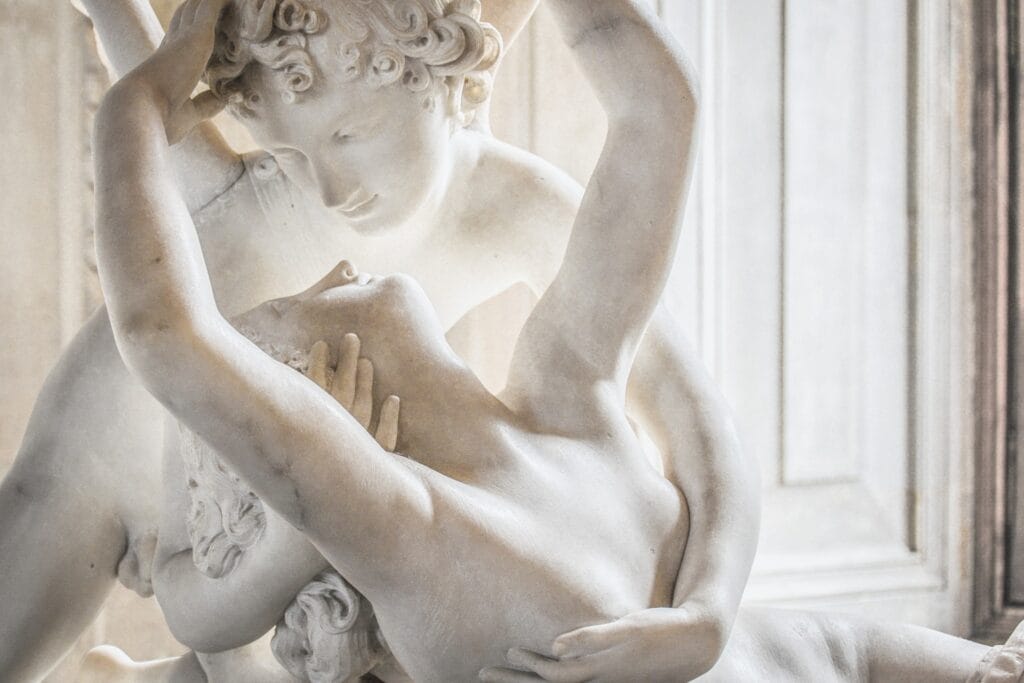 A marble sculpture of an angel gently embracing a woman, who reaches him with her hands. The sculpture illustrates a tender intimate connection between the two. 