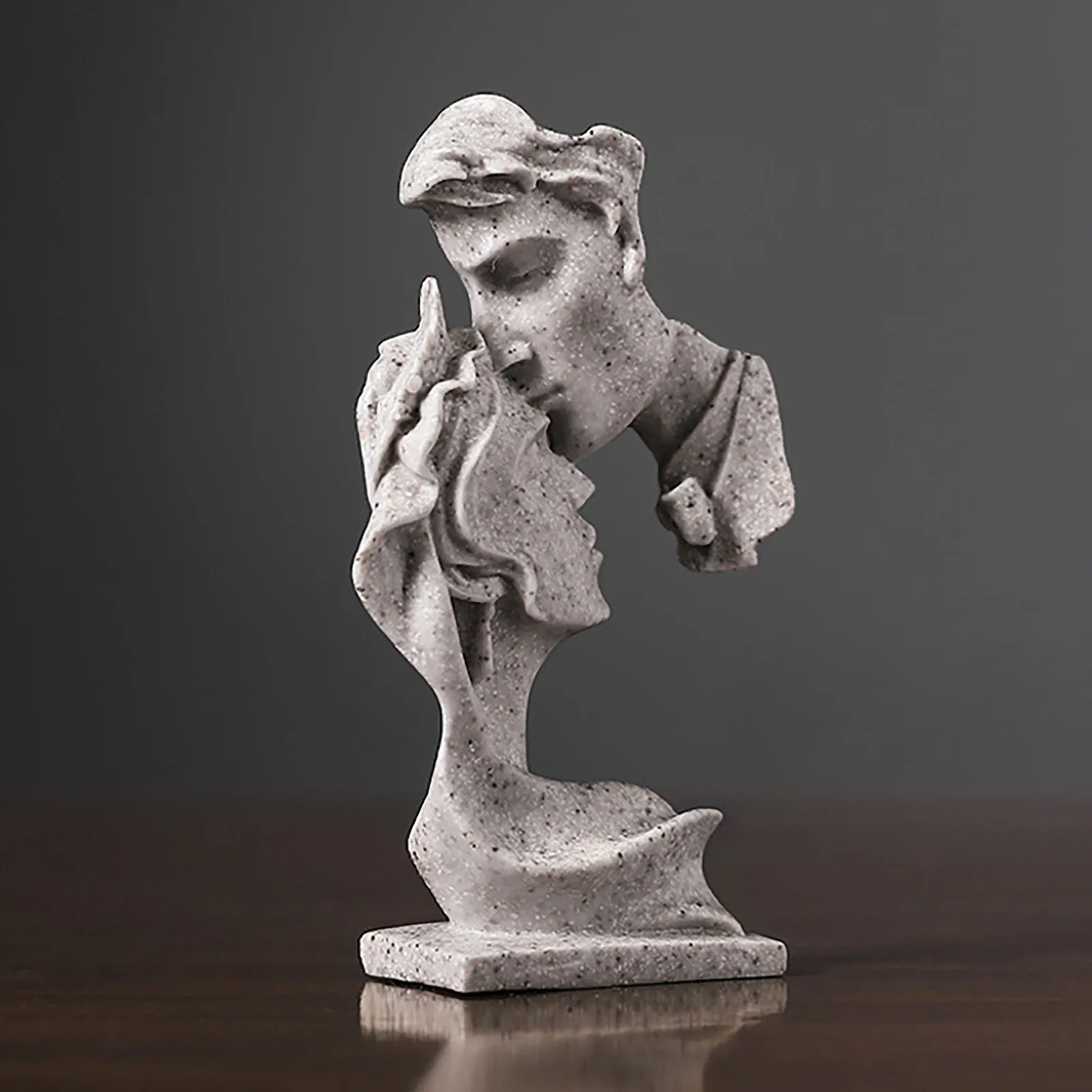 A sculpted gray stone bust, exploring relationships and sexuality, features fragmented male and female figures facing each other. With missing sections and wavy textured surfaces, the piece rests on a wooden base against a gray background.