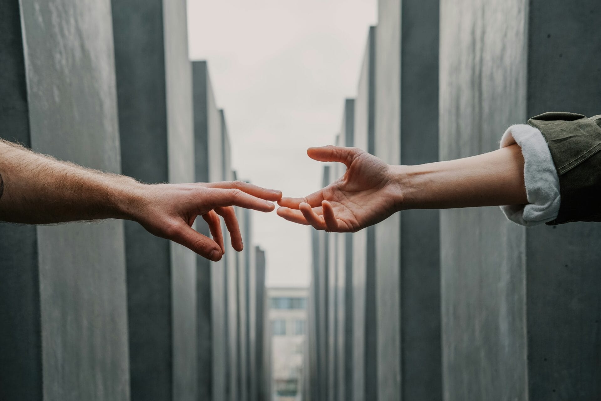 Two hands reaching out to each other against a backdrop of gray concrete structures symbolize a deepest connection between two people. 