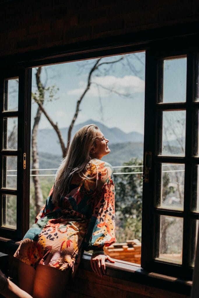 woman in red and white floral long sleeve shirt leaning on the window and embrasing the moment of selflove. 